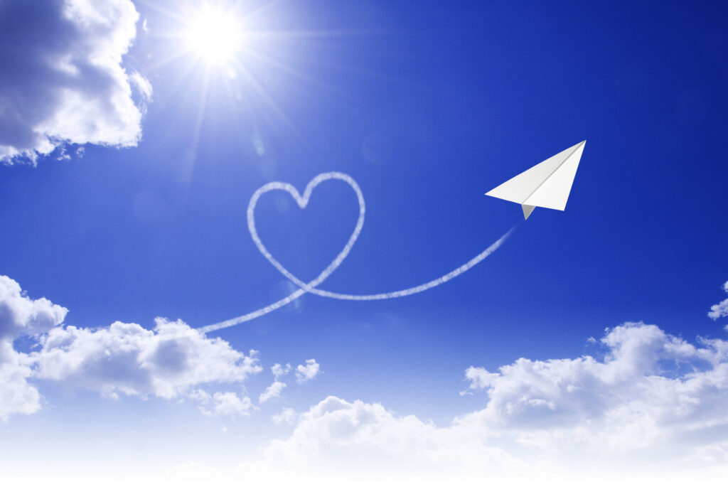 Paper airplane flying across a blue sky with a heart-shaped trail